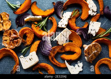 Scheiben von gebackenen Kürbis, Zwiebeln, Knoblauch, Gewürze und Scheiben von Käse Dorblin auf Pergamentpapier und alten blauen Stein Hintergrund. Draufsicht. Stockfoto