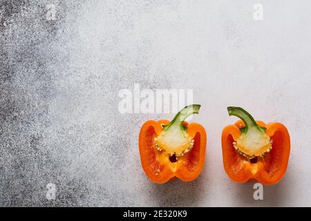 Zwei orange frische Paprika in zwei Hälften auf einem grauen Beton alten Hintergrund geschnitten. Kochkonzept. Draufsicht. Stockfoto