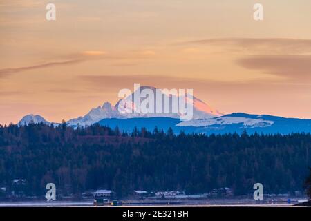 Die ersten Lichtstrahlen treffen auf Mt Baker mit der Küste im Vordergrund. Stockfoto