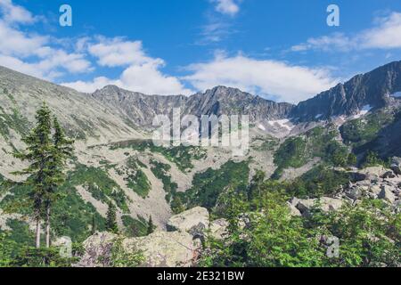 Bergtal mit Steinkamm und Bäumen am Horizont. Reisen Sie im Sommer durch wilde Felsen. Berglandschaft gegen blauen Himmel an sonnigen Tagen Stockfoto