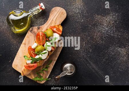 Caprese Bruschetta Toasts mit Kirschtomaten, Mozzarella, Oliven und Basilikum auf altem dunklen Hintergrund. Draufsicht. Stockfoto