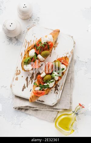 Caprese Bruschetta Toasts mit Kirschtomaten, Mozzarella, Oliven und Basilikum auf weißem Teller alten hellen Hintergrund. Draufsicht. Stockfoto