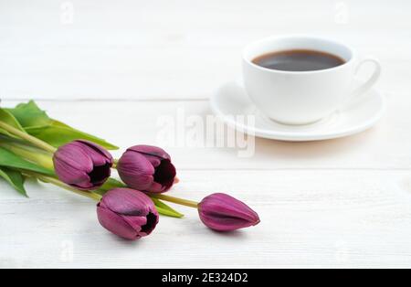 Lila Blumen und eine weiße Kaffeetasse im Hintergrund auf einem hellen Holzhintergrund. Stockfoto