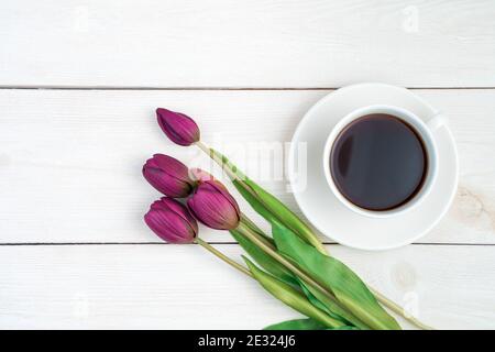 8. März, Tulpen und Kaffee in einer weißen Tasse auf hellem Holzhintergrund. Stockfoto