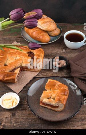 Obstkuchen, Brötchen und ein Strauß Tulpen auf einem Holzhintergrund. Stockfoto