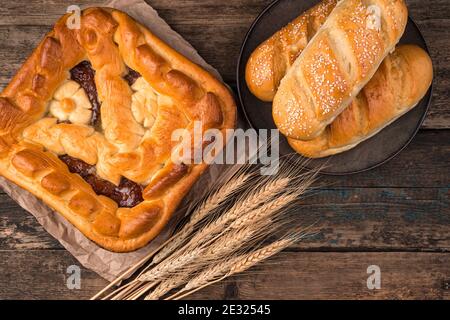 Apfelkuchen, frische Brötchen und Weizenspieß auf braunem Holzhintergrund. Stockfoto