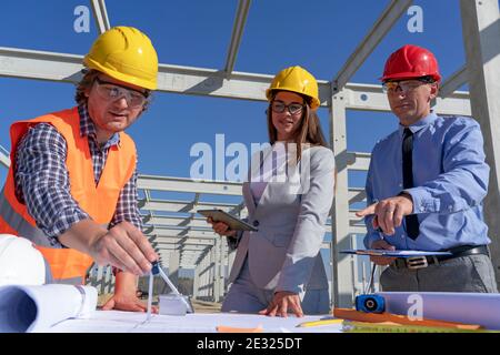 Konstruktionsprojekt Team in Hardhats arbeitet an einem Blueprint. Business, Building, Teamwork und Gleichstellungskonzept. Bau der Fabrik der Zukunft. Stockfoto