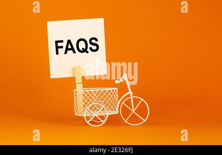 HÄUFIG GESTELLTE FRAGEN, Symbol für häufig gestellte Fragen. Whitepaper. Wörter „FAQS, häufig gestellte Fragen“. Miniaturfahrrad. Schöner orangefarbener Hintergrund. Bus Stockfoto