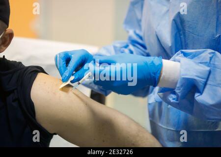 Details mit einem Mann, der eine intramuskuläre Injektion mit dem SARS-Cov-2-Impfstoff in einem Krankenhaus von einem Arzt erhält. Stockfoto