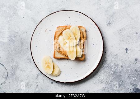 Toast mit Erdnussbutter, Bananenscheiben, Honig und Mandelflocken auf altem grauen Betongrund. Draufsicht. Stockfoto
