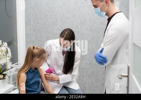 Ein Lehrling im letzten Jahr der Medizin spricht mit einem kleinen Patienten, um keine Angst vor Injektionen zu haben. Der Arzt bereitet sich auf die Injektion des neuen Impfstoffs vor. Stockfoto