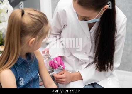 Ein Lehrling im letzten Jahr der Medizin spricht mit einem kleinen Patienten, um keine Angst vor Injektionen zu haben. Der Arzt bereitet sich auf die Injektion des neuen Impfstoffs vor. Stockfoto