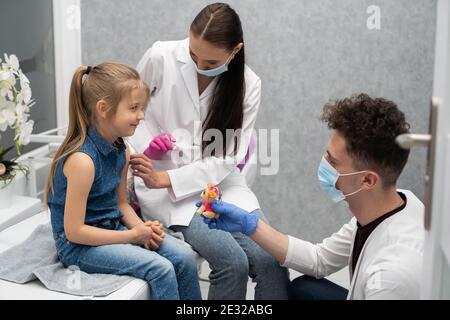 Ein Lehrling im letzten Jahr der Medizin spricht mit einem kleinen Patienten, um keine Angst vor Injektionen zu haben. Der Arzt bereitet sich auf die Injektion des neuen Impfstoffs vor. Stockfoto