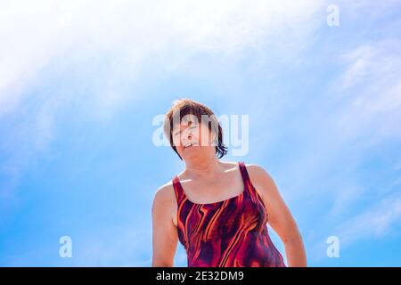 Fröhliche ältere Frau über 65 in einem nassen Badeanzug gegen einen blauen Himmel, lachen und genießen Sie einen Sommertag, Quarantäneende und Selbstisolation Stockfoto