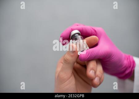 Er hält ein Fläschchen mit einem Medikament und einer Spritze in der Hand und gibt es einem medizinischen Praktikanten, damit er dieses Set zur Herstellung von Impfstoffen und verschiedenen Injektionen, auch und schließlich Viren aus der COVID19-Gruppe, kennenlernen kann. Nahaufnahme. Stockfoto