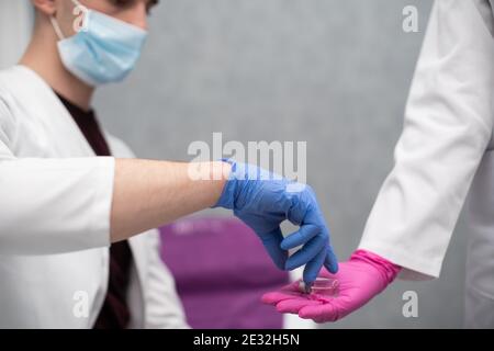 Er hält ein Fläschchen mit einem Medikament und einer Spritze in der Hand und gibt es einem medizinischen Praktikanten, damit er dieses Set zur Herstellung von Impfstoffen und verschiedenen Injektionen, auch gegen Viren aus der COVID19-Gruppe, kennenlernen kann. Stockfoto