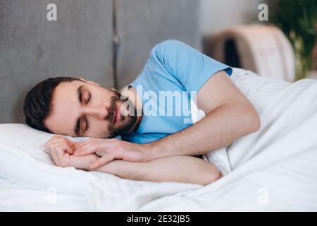 Blick auf einen hübschen, ruhigen Mann mit Bart, der auf dem Kissen liegt und morgens schläft. Stockfoto