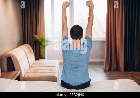 Guten Morgen junger Mann, der im Bett aufwacht und seine Arme streckt, Rückansicht, Kopierraum Stockfoto