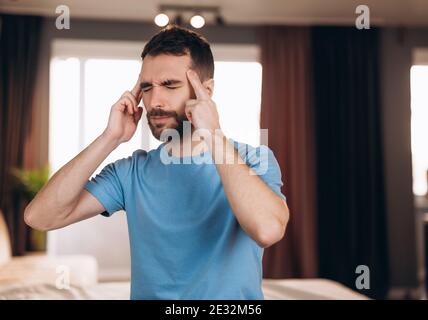 Mann mit Bart sitzt im Bett zu Hause leiden unter Kopfschmerzen oder Kater. Konzept für Schlafenszeit und Ruhe Stockfoto