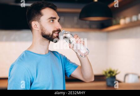 Gesunde Ernährung. Hübscher junger Mann mit Bart, der frisches Wasser in der Flasche trinkt. Konzept Morgen. Stockfoto