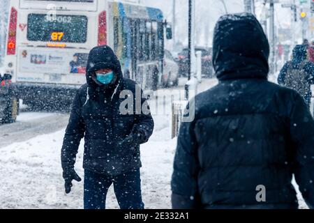 Montreal, CA - 16. Januar 2021: Mann mit Gesichtsmaske zum Schutz vor COVID-19, der während des Schneesturms die Straße entlang läuft Stockfoto