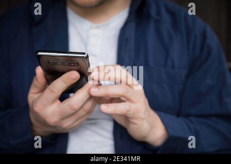Mann in blauem Hemd mit seinem Smartphone, Detail der Hände. Stockfoto