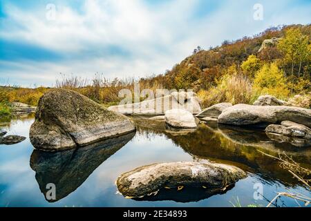 Ein schneller, flacher, sauberer Bach fließt zwischen glatten nassen großen Steinen, umgeben von hohen trockenen Klumpen, die im Wind im malerischen Ukraine schwanken Stockfoto