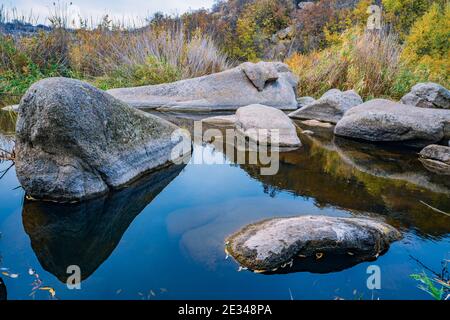 Ein schneller, flacher, sauberer Bach fließt zwischen glatten nassen großen Steinen, umgeben von hohen trockenen Klumpen, die im Wind im malerischen Ukraine schwanken Stockfoto