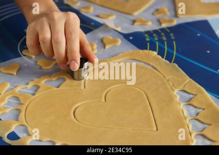 Frau mit einer Form schneidet Herzen für Kekse aus Teig. Kochen hausgemachten herzförmigen Kuchen. Schritt-für-Schritt-Anleitung Stockfoto
