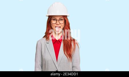 Junge Rotschopf Frau trägt Architekt Hardhat aufragend Zunge aus glücklich mit lustigen Ausdruck. Emotion Konzept. Stockfoto