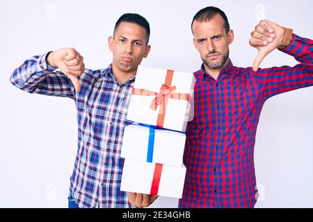 Junge Homosexuell paar von zwei Männern halten Geschenk mit wütenden Gesicht, negative Zeichen zeigt Abneigung mit Daumen nach unten, Ablehnung Konzept Stockfoto