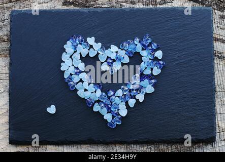 Viele kleine blaue Glasherzen in Form eines Herz auf Stein Stockfoto