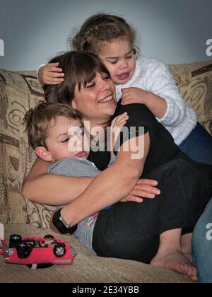 Glückliche Mutter mit Sohn und Tochter sitzen Umarmung auf der Sofa und Fernsehen Stockfoto