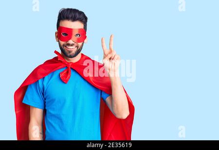Junger schöner Mann mit Bart trägt Superhelden Kostüm zeigt und zeigt mit den Fingern Nummer zwei, während lächelnd zuversichtlich und glücklich. Stockfoto