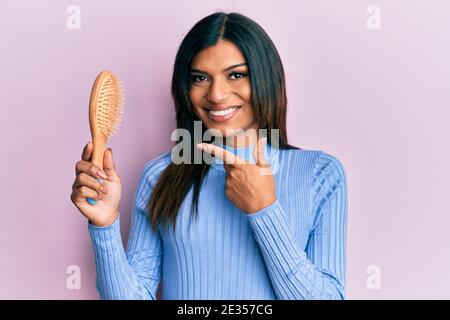 Junge lateinische transsexuelle Transgender Frau mit Haarbürste lächelnd glücklich zeigen Mit Hand und Finger Stockfoto