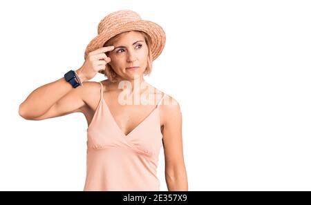 Junge blonde Frau trägt Sommerhut zeigt unglücklich Pickel auf der Stirn, hässliche Infektion der Mitesser. Akne und Hautproblem Stockfoto