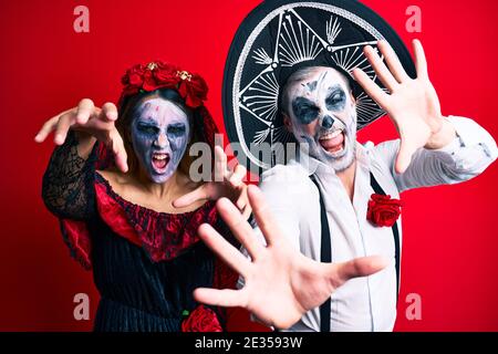 Schönes Paar trägt Tag der Toten Kostüm gestikuliert als Zombie über isolierten roten Hintergrund. Stockfoto