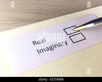 Eine Person beantwortet die Frage auf einem Blatt Papier. Die Person denkt, real oder imaginär zu sein. Stockfoto