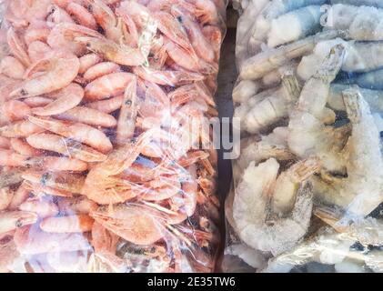 Zwei große Plastiktüten mit gefrorenen rohen und gekochten Garnelen, auf der Theke des Fischmarktes. Stockfoto