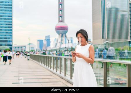 Telefon Asian mittleren Alters elegante Frau mit Smartphone SMS auf Shanghai City Street. Der Lebensstil der reifen Menschen. Geschäftsfrau mit Mobiltelefon Stockfoto