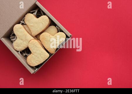 Herzförmige Valentinskekse in einer Kraft-Geschenkbox auf rotem Hintergrund. Flaches Futter. Speicherplatz kopieren. Stockfoto