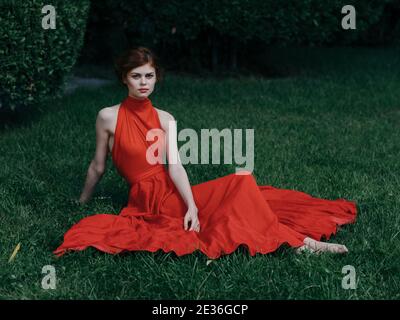 Frau in roten Kleid sitzt auf dem Gras Charme und Luxuriöser Park im exotischen Stil Stockfoto