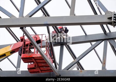 Der Mann Schweißer, der am Kran arbeitet, führt die Hochhausarbeiten auf den Schweißmetallkonstruktionen des neuen Turms in der Höhe durch. Isoliert auf weißem Hintergrund. Stockfoto