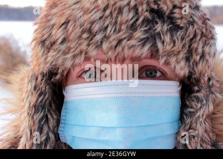 Porträt einer Person in einem Pelzmütze und blaue Einweg-Gesichtsmaske. Frau in Pelzhut und Pandemie chirurgische Maske während Coronavirus Quarantäne im Freien Stockfoto