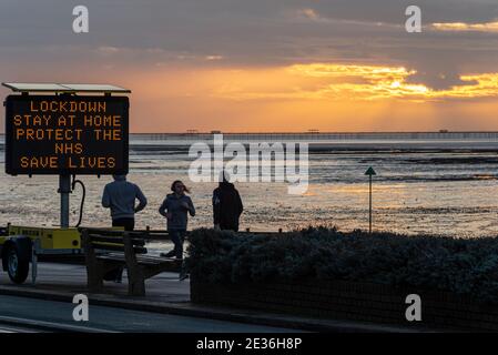 Southend on Sea, Essex, Großbritannien. Januar 2021. Eine Wolkenbank hat den Sonnenaufgang bedeckt, bewegt sich aber weg, um Platz für einen hellen Morgen zu machen. Menschen sind aus Sport und Hund zu Fuß in der Morgendämmerung, vorbei an einem elektronischen Matrix-Zeichen warnt die Menschen zu Hause in Bezug auf die COVID 19 Lockdown Richtlinien zu bleiben. Lockdown drei in Großbritannien. Jogger und Spaziergänger an der Strandpromenade Stockfoto