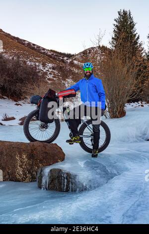 Bärtiger männlicher Reisender auf einem Fahrrad im Winter in den Bergen. Reisen im Winter. Hochplateau Turgen-ASY, Kasachstan Stockfoto