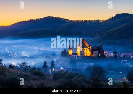 Biertan, Rumänien. Nebliger Sonnenuntergang im sächsischen Dorf mit der befestigten Kirche, Siebenbürgen. Stockfoto