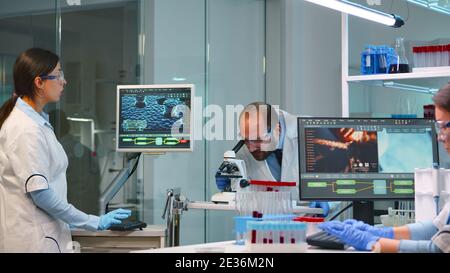 Man-Forscher Blick auf Proben unter dem Mikroskop, während Krankenschwester schreibt Informationen auf pc in modern ausgestatteten Labor. Ärzte arbeiten mit verschiedenen Bakterien, Gewebe und Blutuntersuchungen Stockfoto