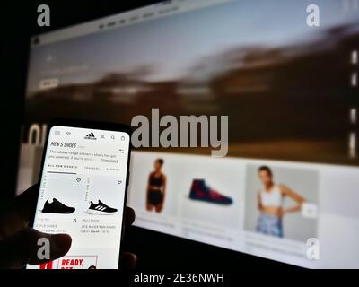 Person scrollt durch den Online-Shop des deutschen Sportartikelherstellers Adidas (Schuhe, Bekleidung, Accessoires). Konzentrieren Sie sich auf den Bildschirm des Mobiltelefons. Stockfoto