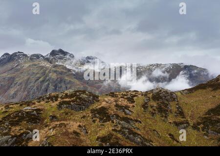 Epische fliegende Drohne Landschaftsbild von Langdale Hechte und Tal Im Winter mit niedrigen Wolken und Nebel wirbeln herum Stockfoto